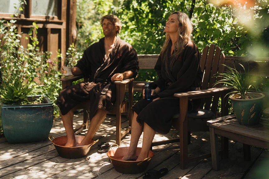 couple in robes enjoying foot bath outside on wooden porch